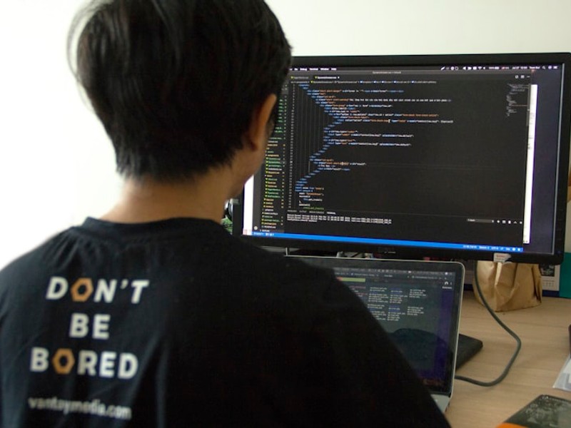 man in black shirt using laptop computer and flat screen monitor